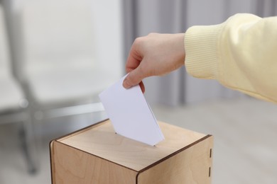 Photo of Woman putting her vote into ballot box on blurred background, closeup