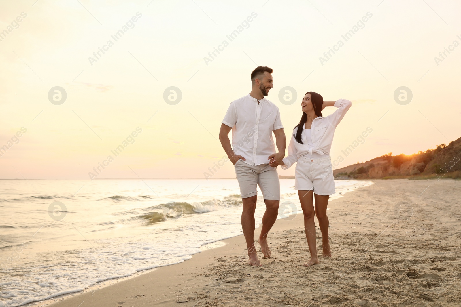 Photo of Happy young couple walking together on beach at sunset