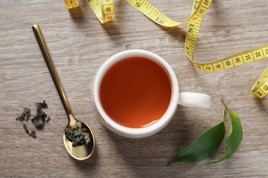 Photo of Cup of herbal diet tea and measuring tape on wooden table, flat lay. Weight loss concept