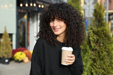 Photo of Happy young woman in stylish black sweater with cup of coffee outdoors