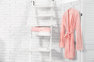 Shelving unit with clean towels and robe near brick wall