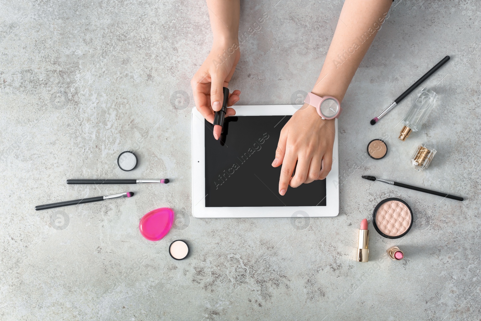 Photo of Young woman with makeup products using tablet at table. Beauty blogger