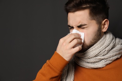 Handsome young man blowing nose against dark background. Space for text