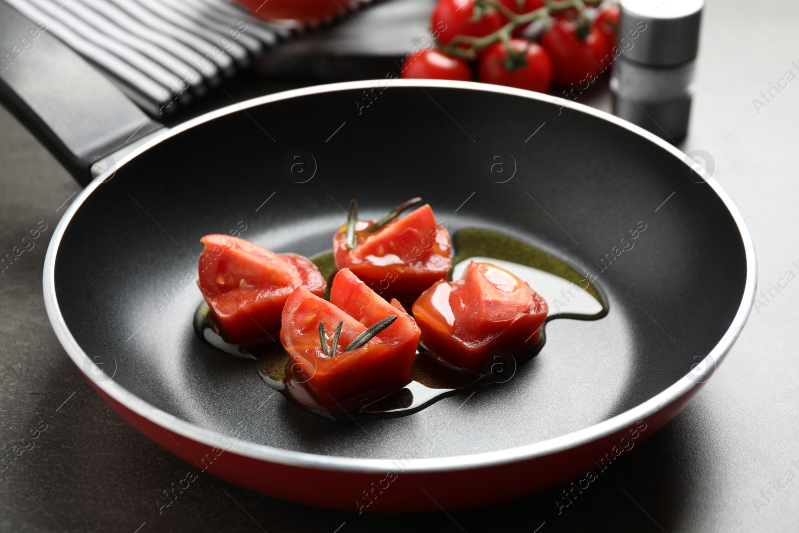 Photo of Melting ice cubes with tomatoes, oil and rosemary on grey table