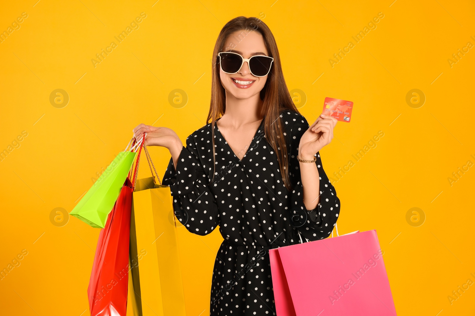 Photo of Happy young woman with shopping bags and credit card on yellow background. Big sale