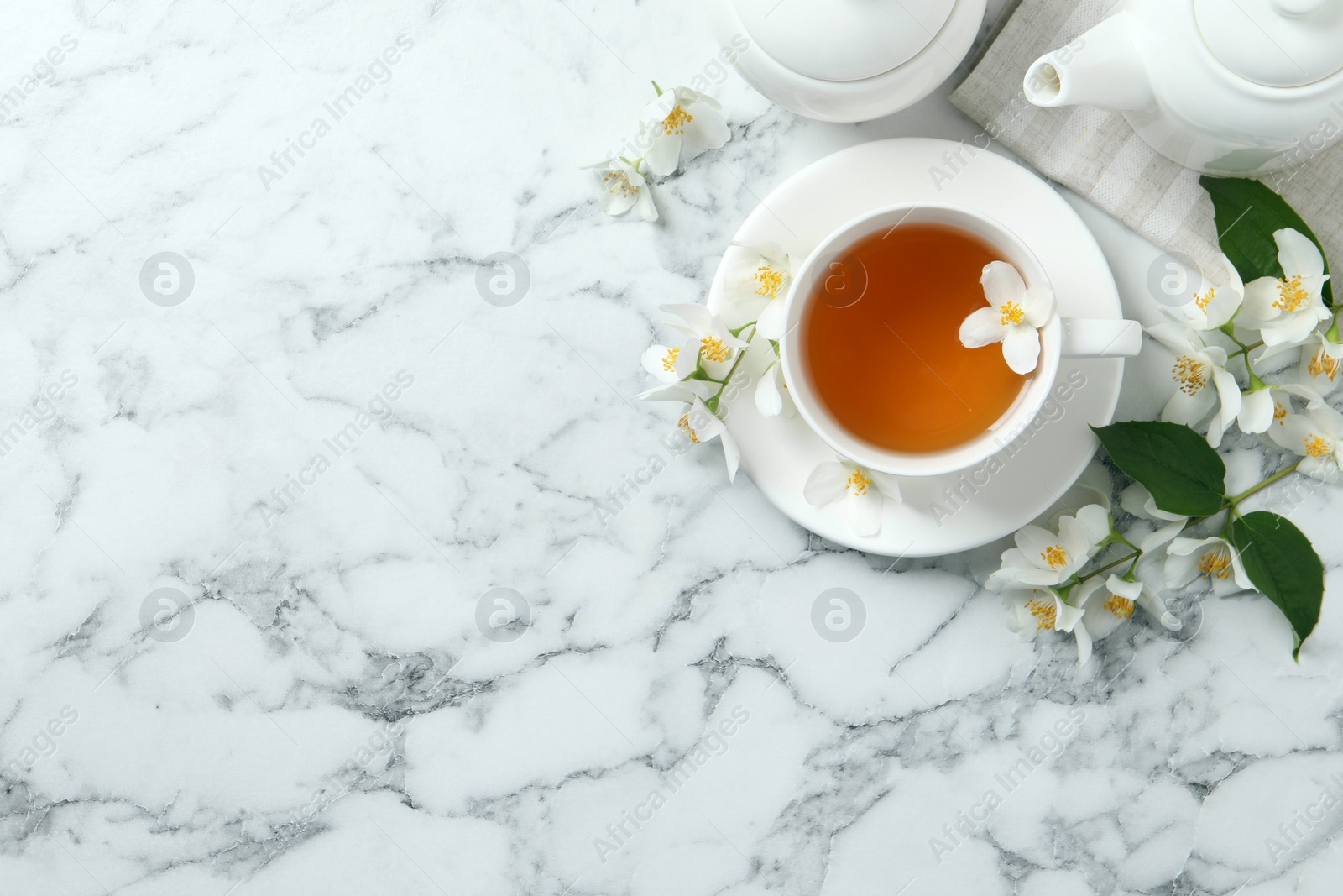 Photo of Aromatic jasmine tea and fresh flowers on white marble table, flat lay. Space for text