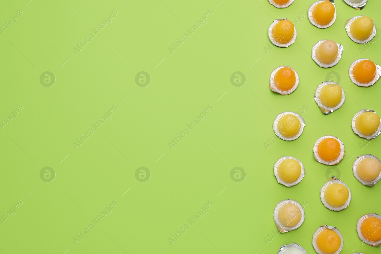 Photo of Tasty bright jelly cups on green background, flat lay. Space for text