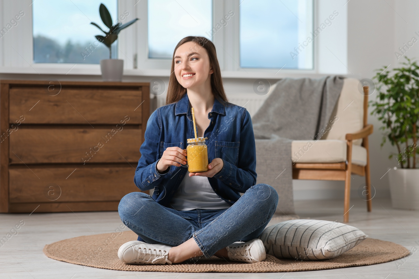 Photo of Beautiful young woman with delicious smoothie on floor at home