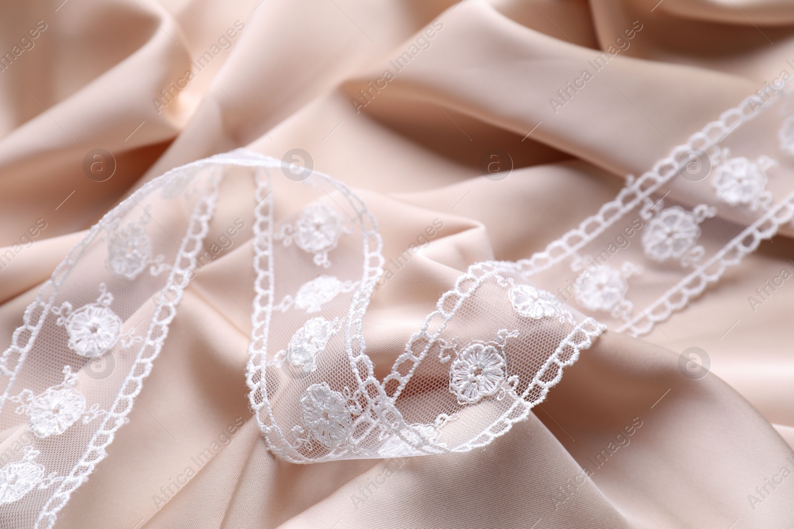 Photo of Beautiful white lace on beige fabric, closeup