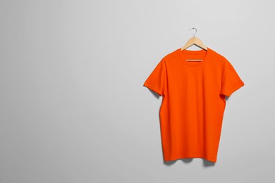 Photo of Hanger with orange t-shirt on light wall. Mockup for design