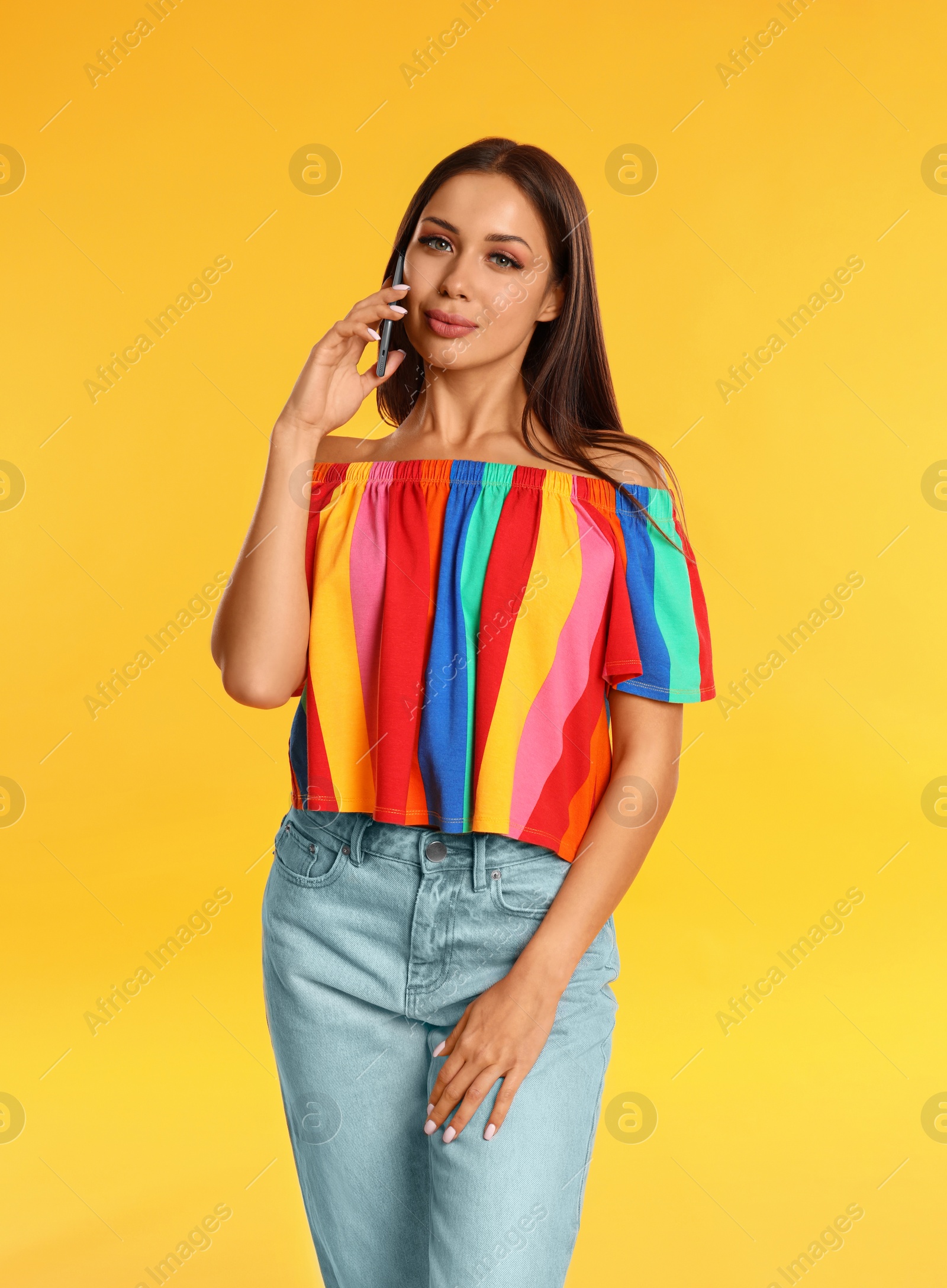 Photo of Beautiful young woman talking by phone on yellow background