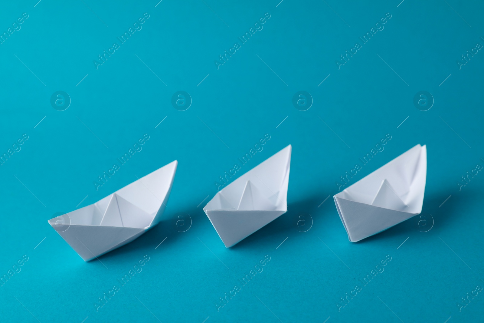 Photo of Handmade white paper boats on light blue background.  Origami art