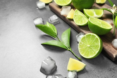 Photo of Composition with fresh ripe limes and ice cubes on gray background