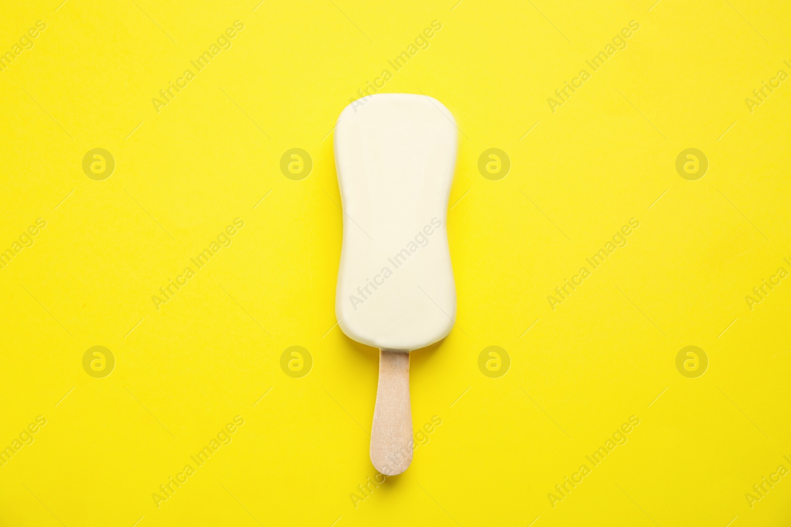 Photo of Ice cream with glaze on yellow background, top view