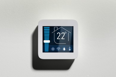 Image of Thermostat displaying temperature in Celsius scale and different icons. Smart home device on white wall
