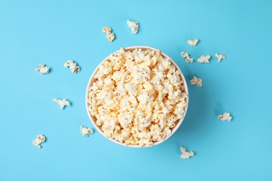 Paper cup with tasty popcorn on color background, top view