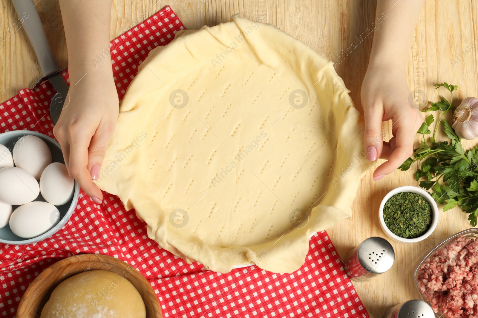 Photo of Woman putting dough for meat pie into baking dish at wooden table, top view