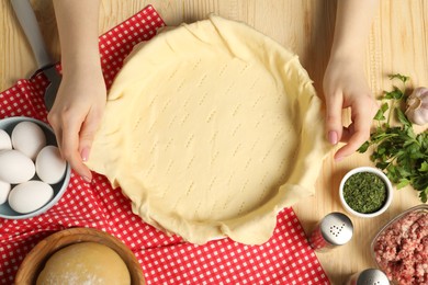 Woman putting dough for meat pie into baking dish at wooden table, top view