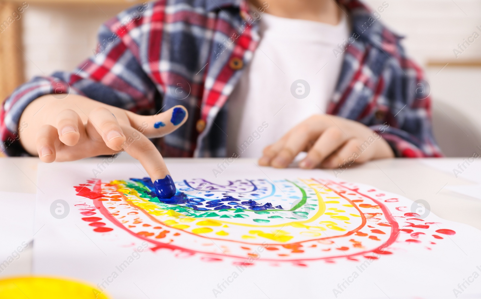 Photo of Little boy painting with finger at white table indoors, closeup