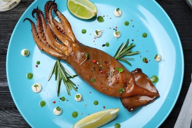 Delicious grilled squid served on black wooden table, flat lay