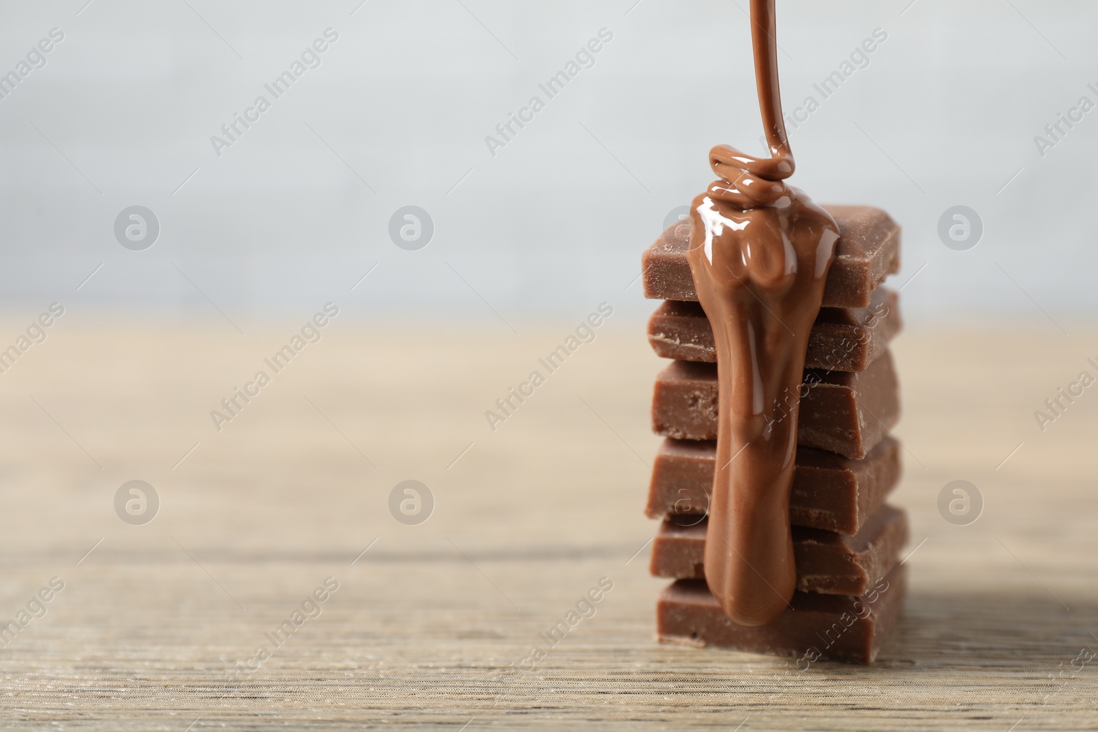 Photo of Pouring tasty milk chocolate paste onto pieces on wooden table, closeup. Space for text