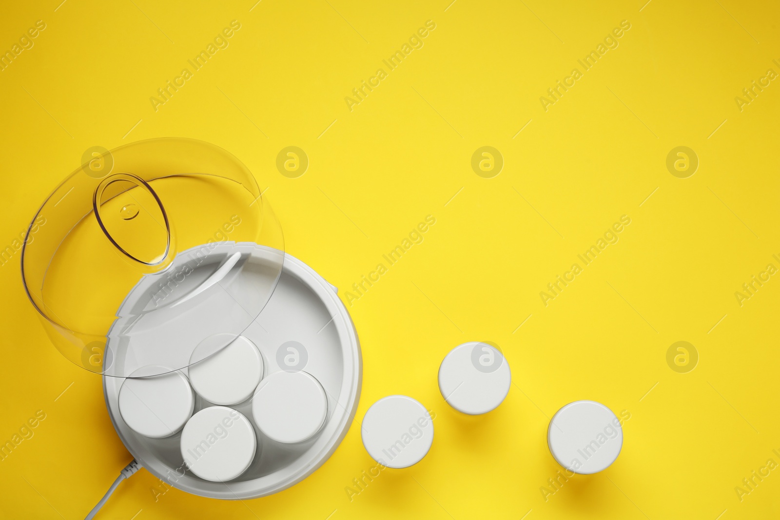 Photo of Modern yogurt maker with jars on yellow background, flat lay. Space for text