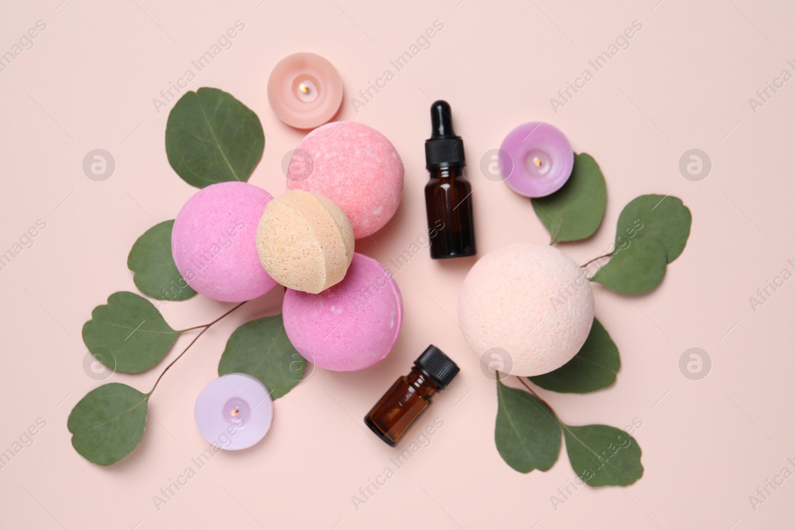 Photo of Bath bombs, eucalyptus leaves, burning candles and bottles on beige background, flat lay