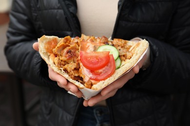 Photo of Woman holding delicious bread with roasted meat and vegetables, closeup. Street food