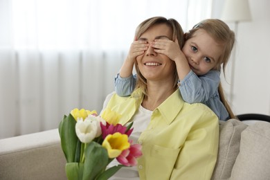 Little girl surprising her mom with bouquet of tulips at home, space for text. Happy Mother`s Day