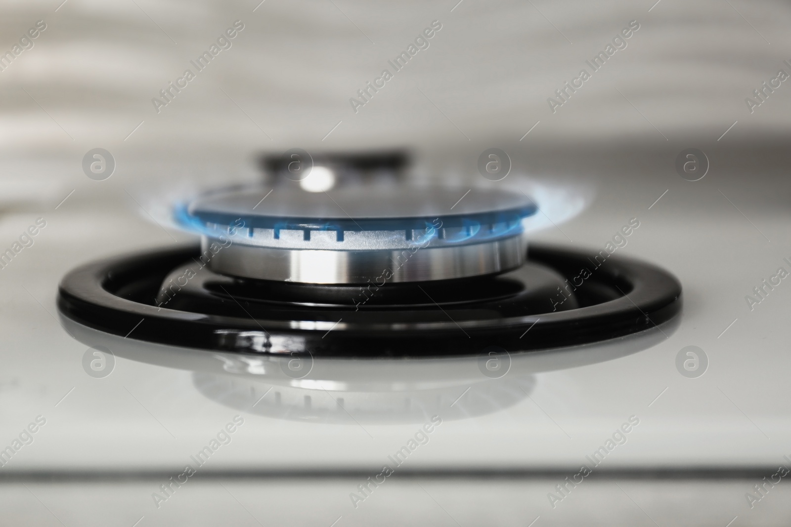 Photo of Gas burner with blue flame on modern stove, closeup