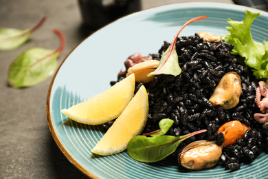Delicious black risotto with seafood and lemon on plate, closeup