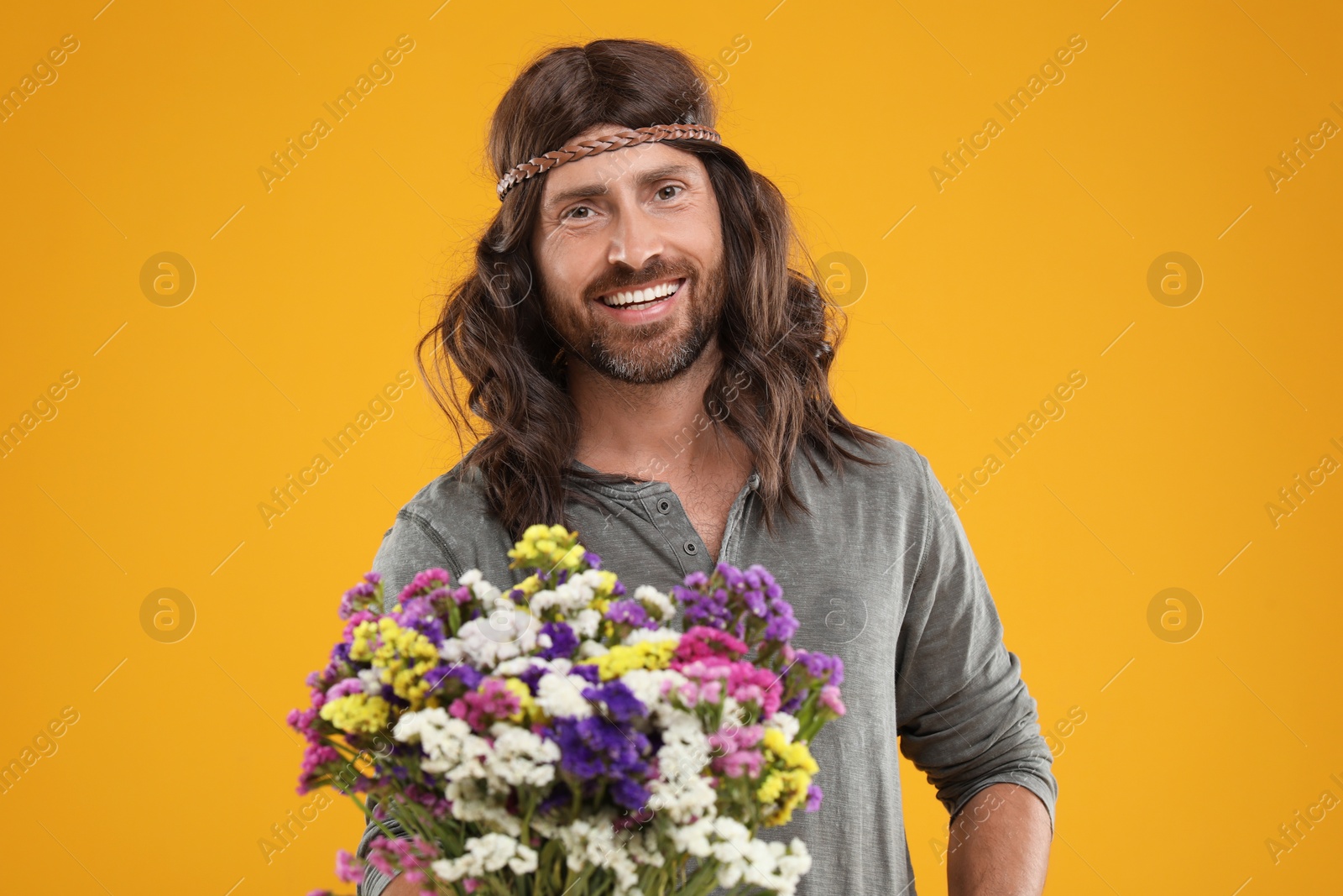 Photo of Hippie man with bouquet of colorful flowers orange background