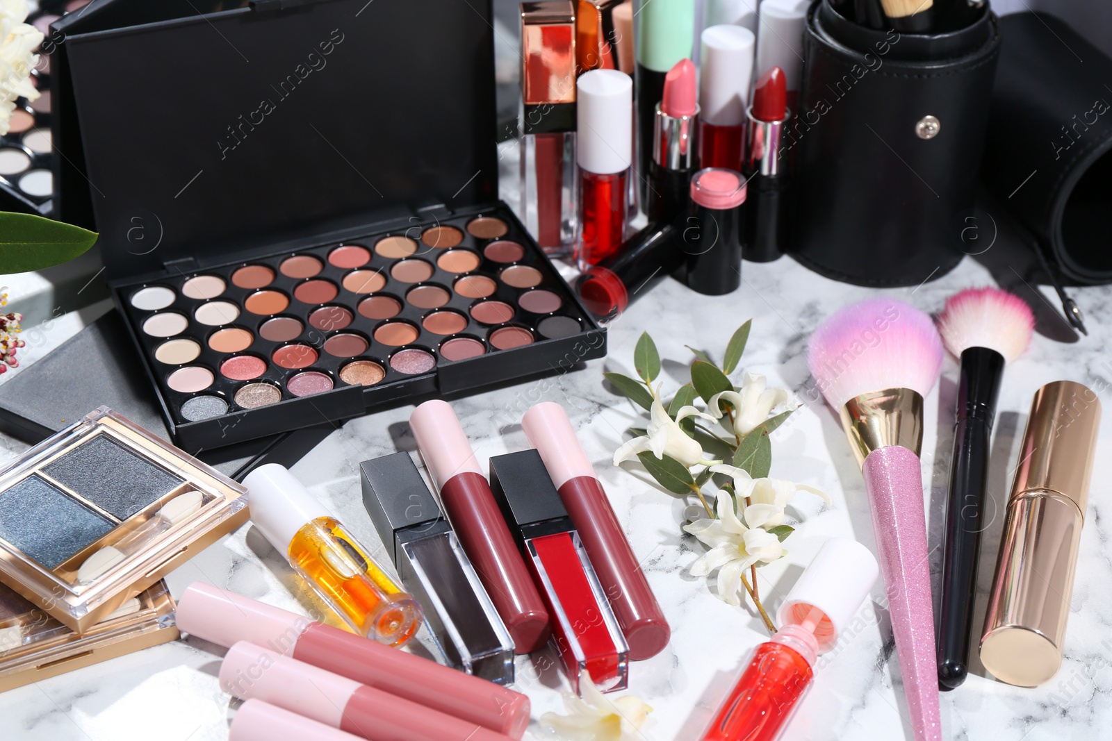 Photo of Bright lip glosses among different cosmetic products on white dressing table