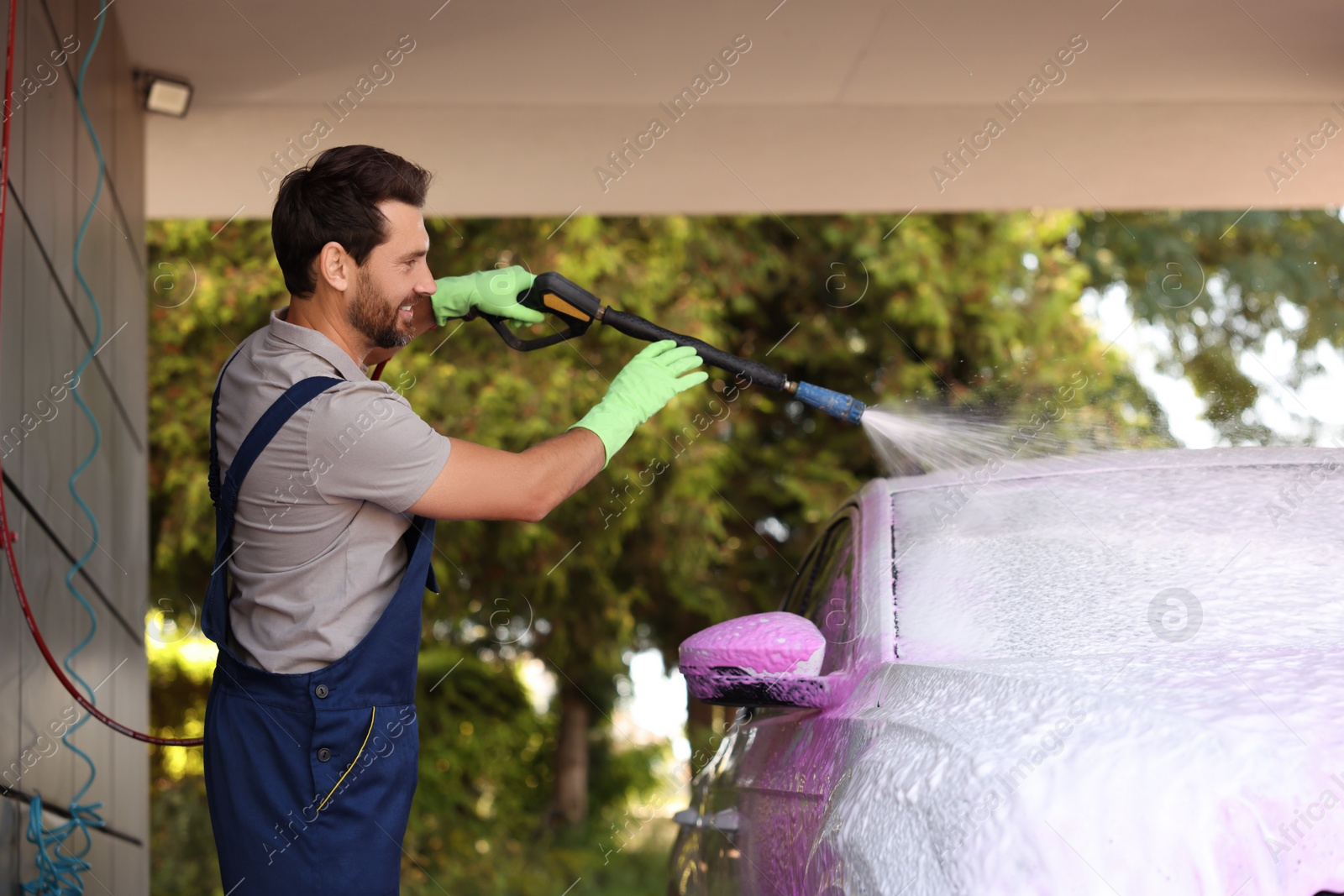 Photo of Worker washing auto with high pressure water jet at outdoor car wash