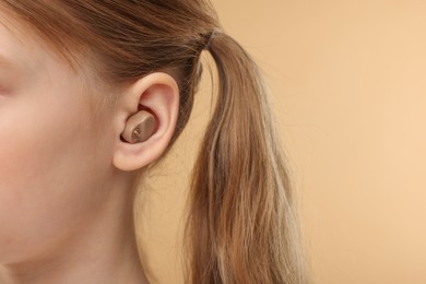 Little girl with hearing aid on pale brown background, closeup. Space for text