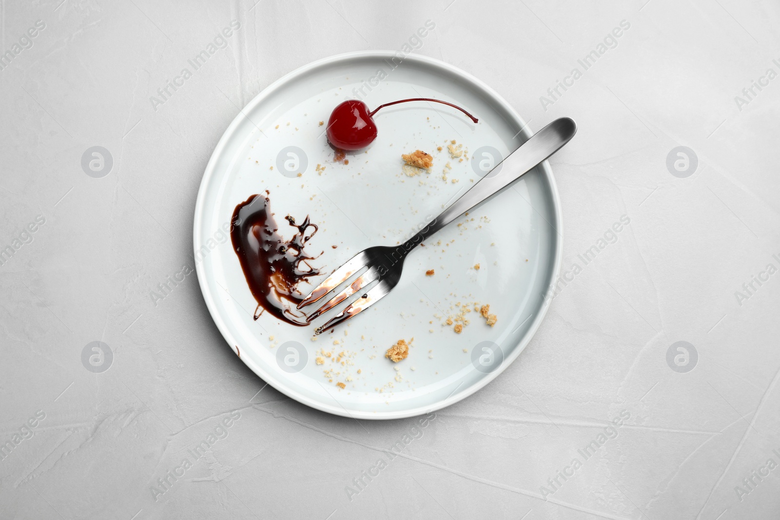 Photo of Dirty plate with food leftovers, fork and canned cherry on grey background, top view