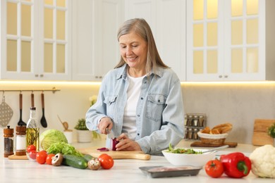 Photo of Happy woman cutting onion at table in kitchen