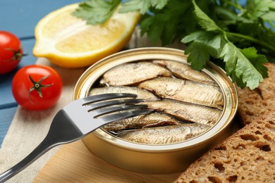 Photo of Tin can with tasty sprats served on wooden board, closeup