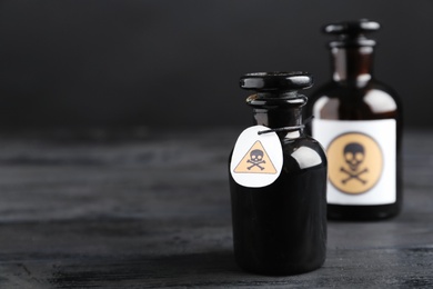 Photo of Glass bottles of poison with warning signs on black wooden table. Space for text