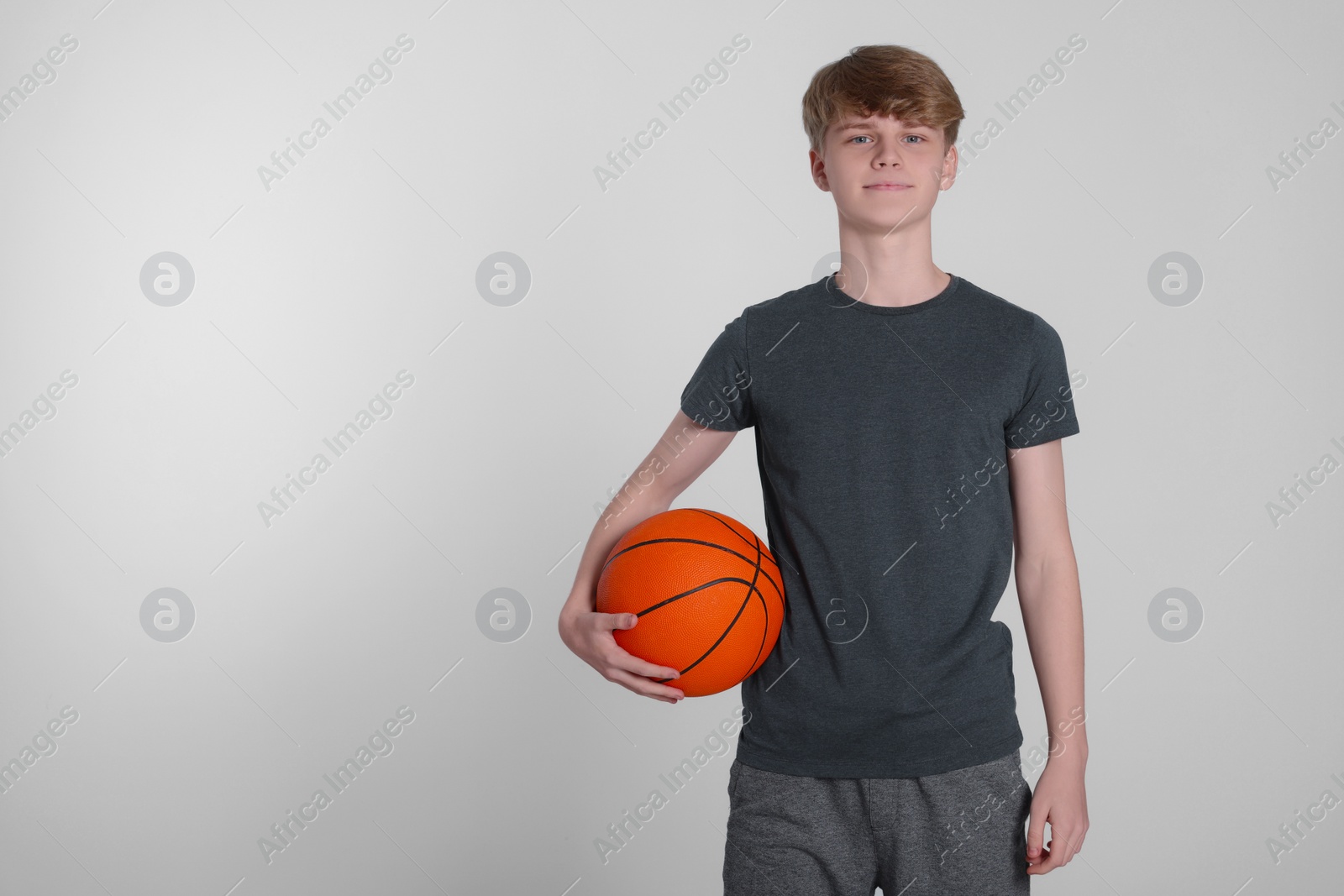 Photo of Teenage boy with basketball ball on light grey background. Space for text