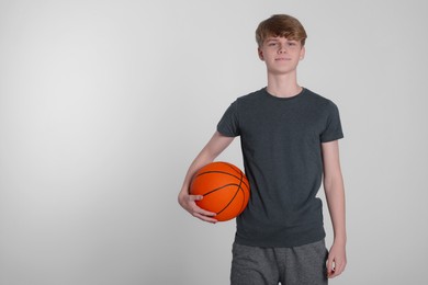 Photo of Teenage boy with basketball ball on light grey background. Space for text