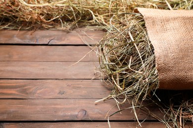Photo of Burlap sack with dried hay on wooden table. Space for text