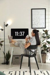 Photo of Young woman with cup of tea at table in light room. Home office