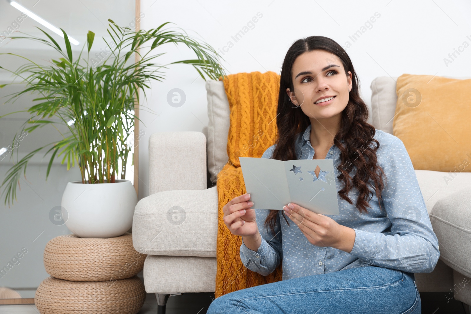 Photo of Young woman with greeting card on floor in living room