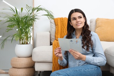 Young woman with greeting card on floor in living room