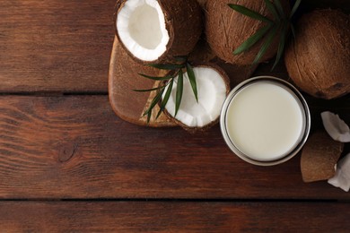 Glass of delicious vegan milk, coconut pieces and palm leaves on wooden table, flat lay. Space for text