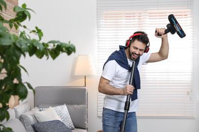 Young man having fun while vacuuming at home