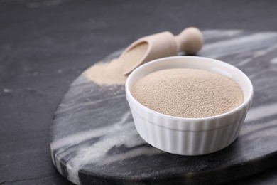 Bowl and scoop with active dry yeast on black table, closeup. Space for text