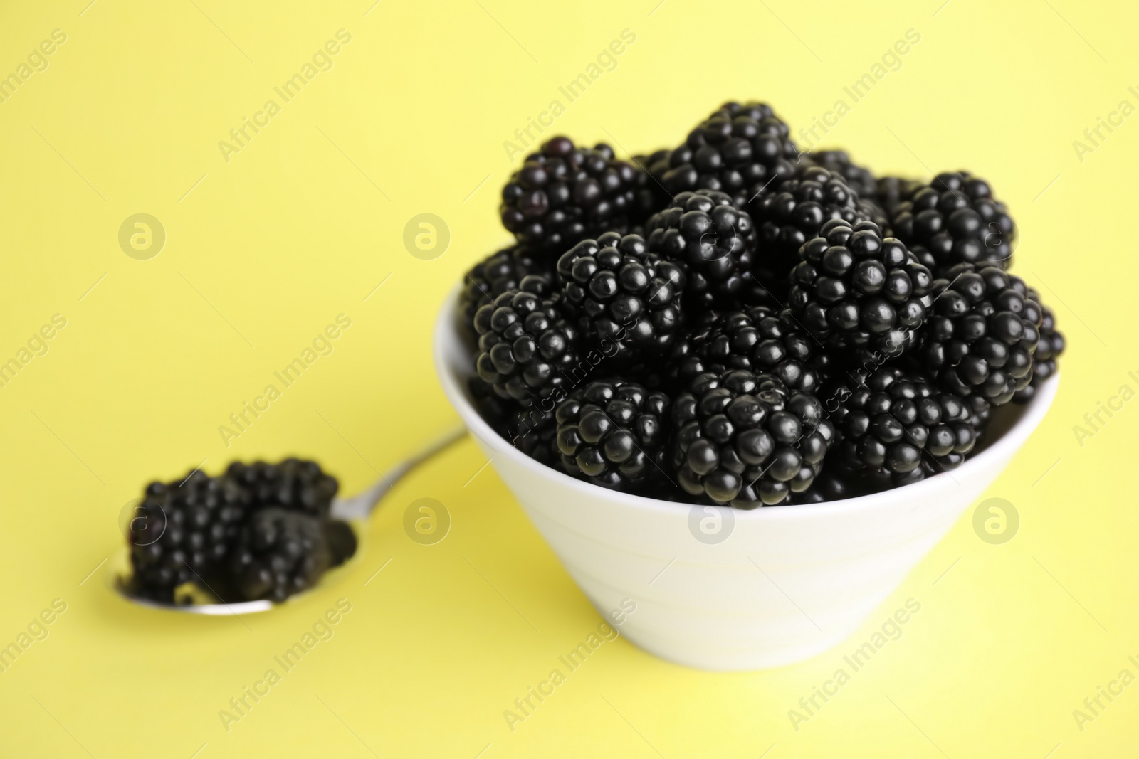 Photo of Fresh ripe blackberries in bowl on yellow background