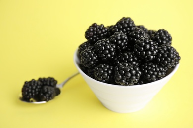Photo of Fresh ripe blackberries in bowl on yellow background